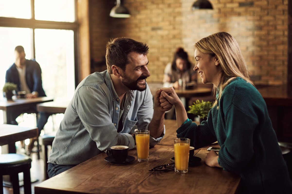 Happy couple holding hands and talking in a cafe. Maneja tu lenguaje corporal