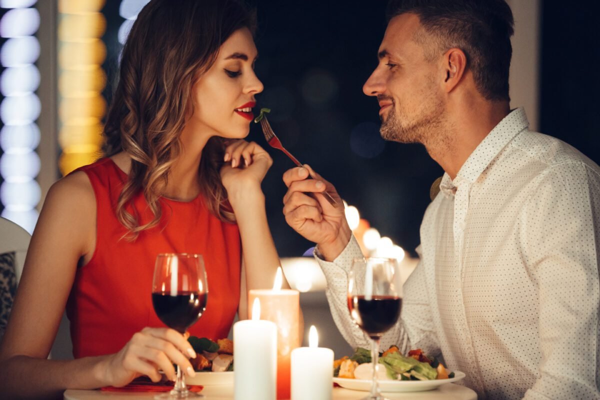 Smiling careful man feed his pretty girlfriend while have romantic dinner at home Hombre y mujer en cita romántica